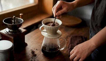Hands pouring water over fresh coffee grounds in dripper