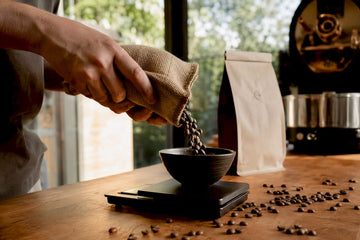 Hand pouring roasted coffee beans into scale bowl