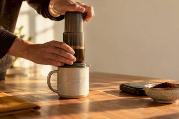 Hands pressing coffee into a ceramic mug